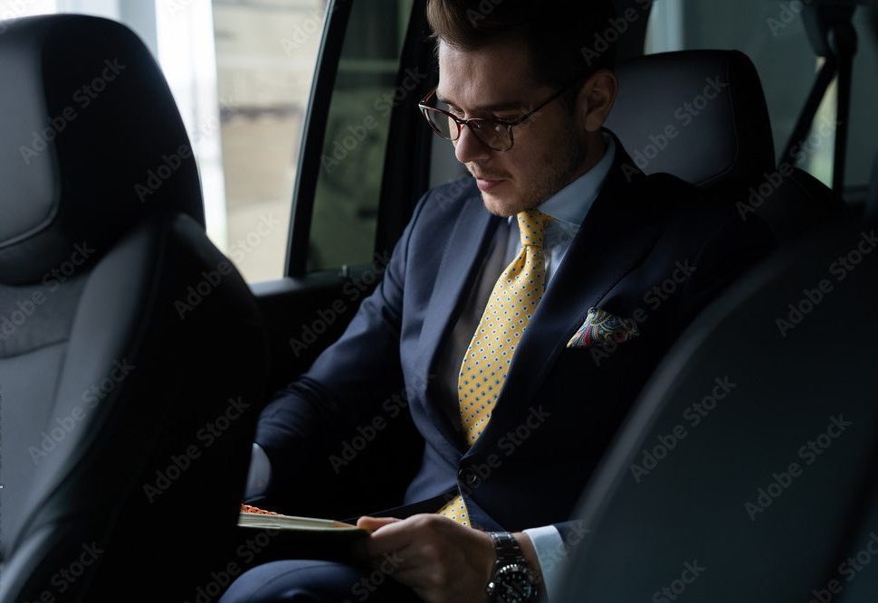 A professional businessman in a dark suit, gold tie, and glasses reading a document in the backseat of a luxury black car, representing Gateway Limousine's executive car service in St. Louis and Chesterfield.