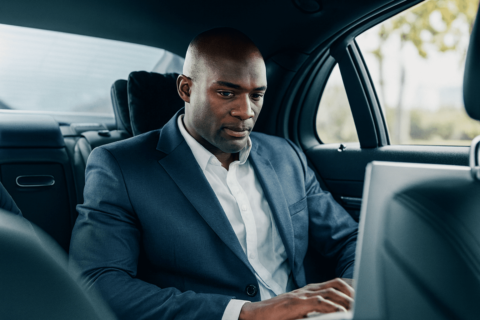 A professional businessman in a tailored blue suit working on a laptop in the back of a luxury black car, illustrating the executive transportation services offered by Gateway Limousine.
